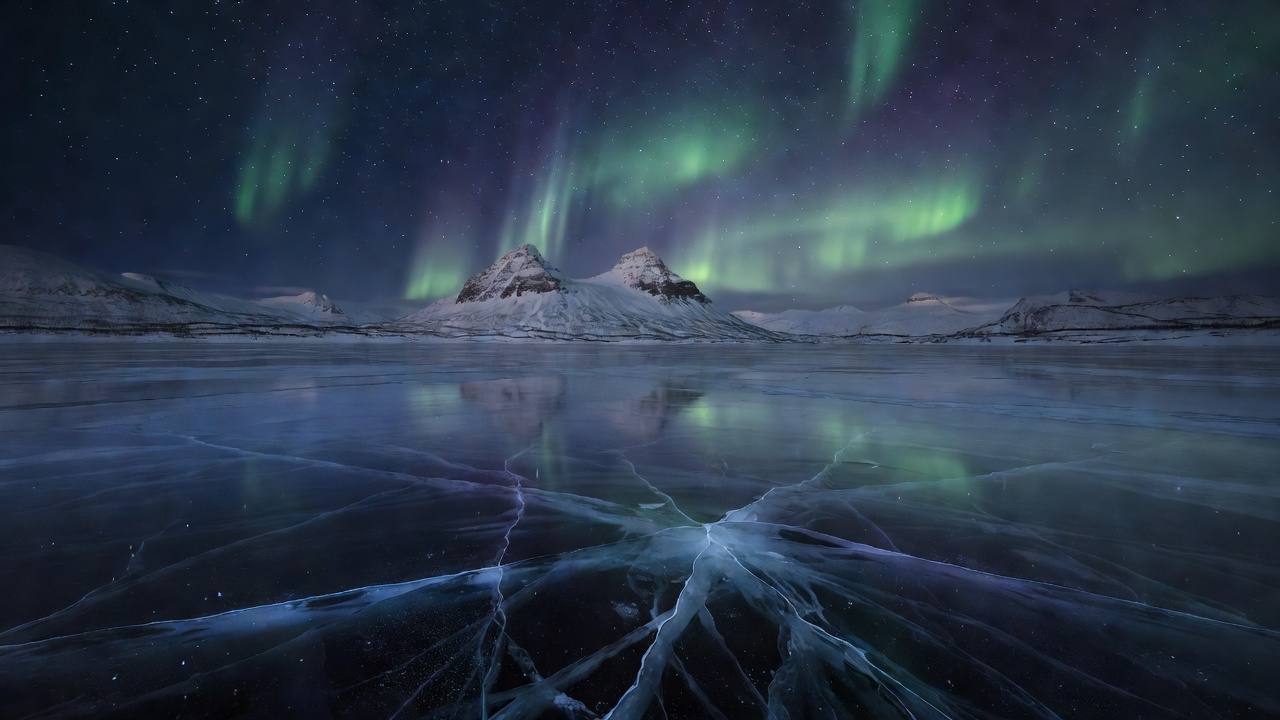 Snow-covered ice of Lake Torneträsk near Abisko under a deep blue night sky with distant mountains